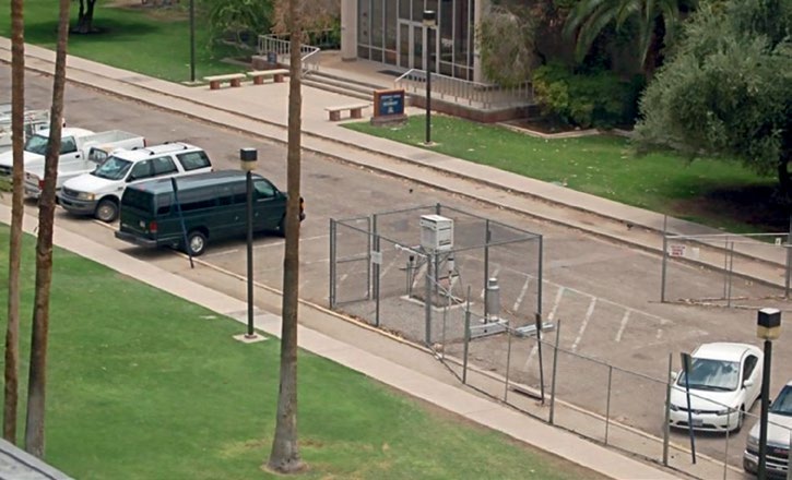 Station météorologique officielle installée dans un stationnement asphalté de l’Université de l’Arizona, entourée de voitures